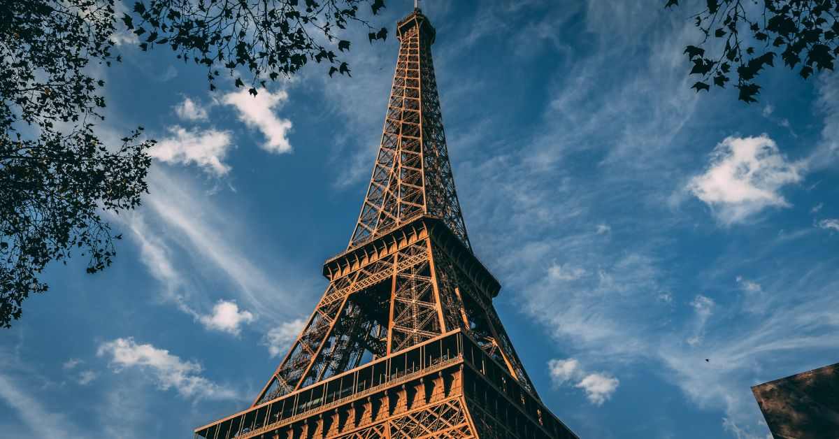 "Eiffel Tower in Paris against a bright blue sky with scattered clouds"