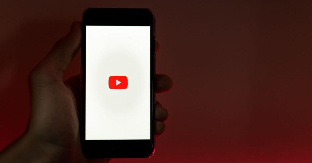 Hand holding a smartphone showing the YouTube logo on a red background.