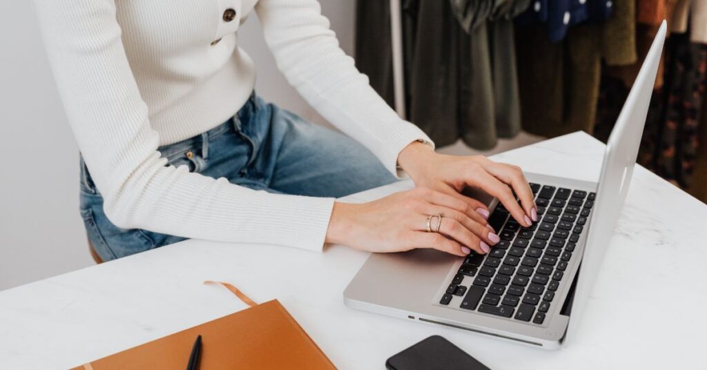 Person typing on laptop at desk with notebook and phone nearby