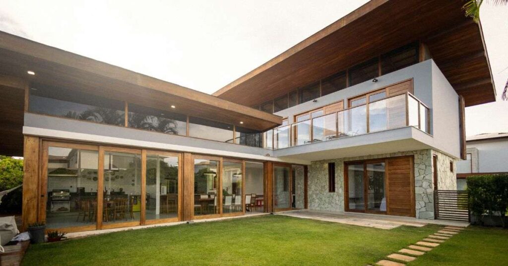 Modern luxury house exterior with wooden architecture, glass windows, and a green lawn in front.