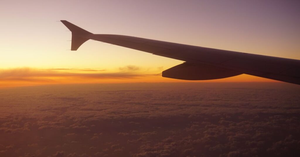 Airplane wing view during sunset flight above clouds.