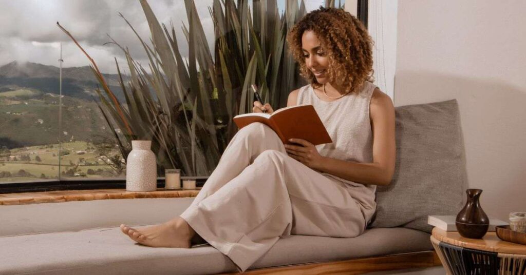 Woman writing in notebook by window in cozy indoor setting.