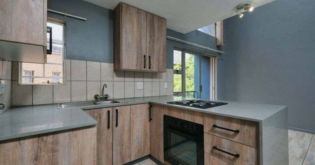 Modern empty kitchen interior with wooden cabinets, countertop, stove, sink, and natural light from windows.