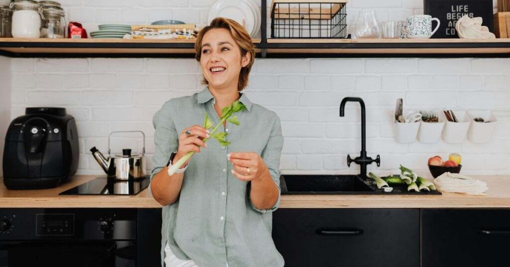 Smiling woman preparing fresh herbs in a modern kitchen with clean countertops and sink.